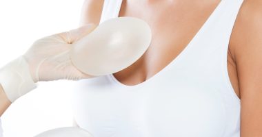 Female doctor choosing mammary prosthesis with her patient over white background.